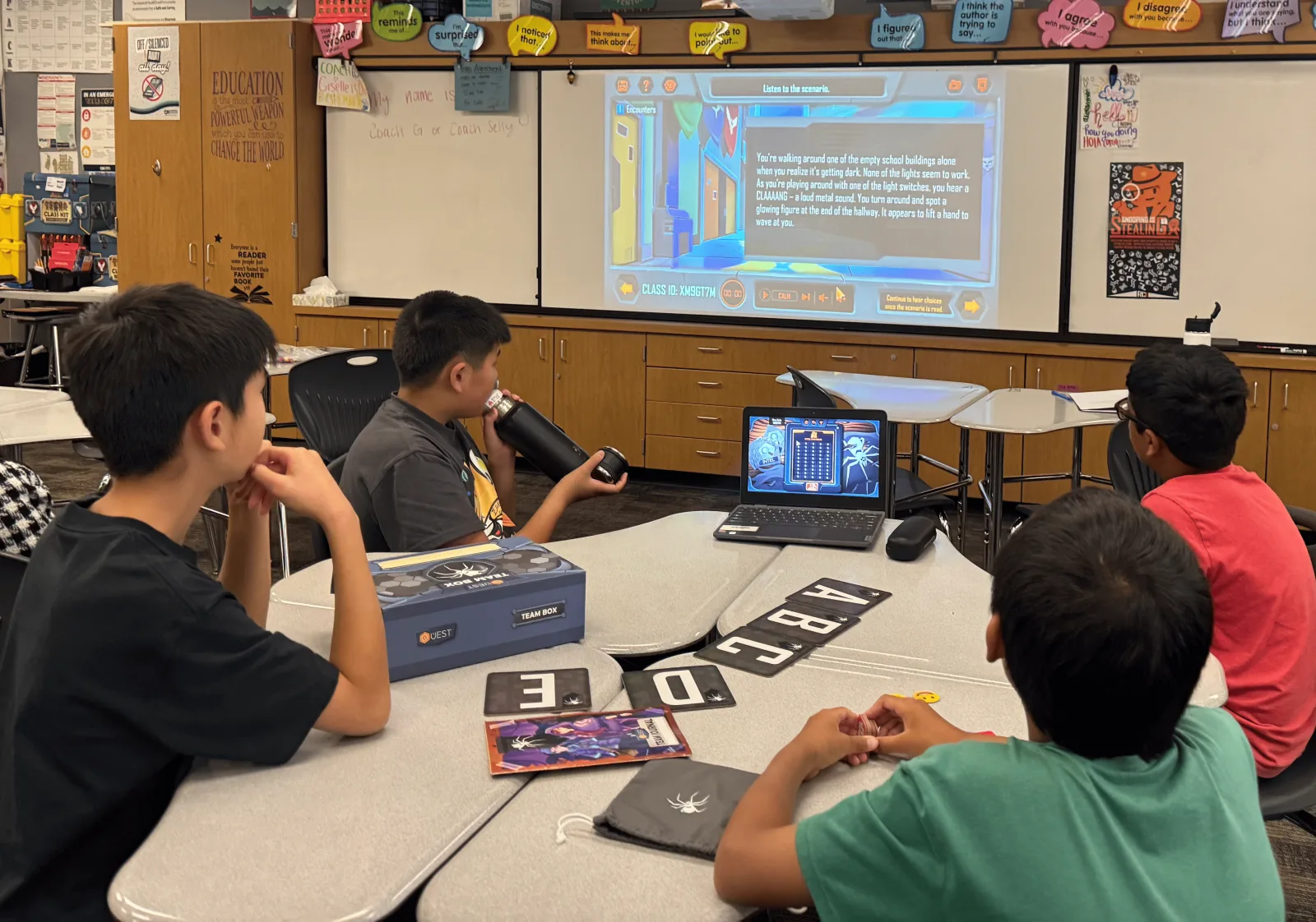 Students at a table with a QUEST team box and letter cards following a narrated scenario